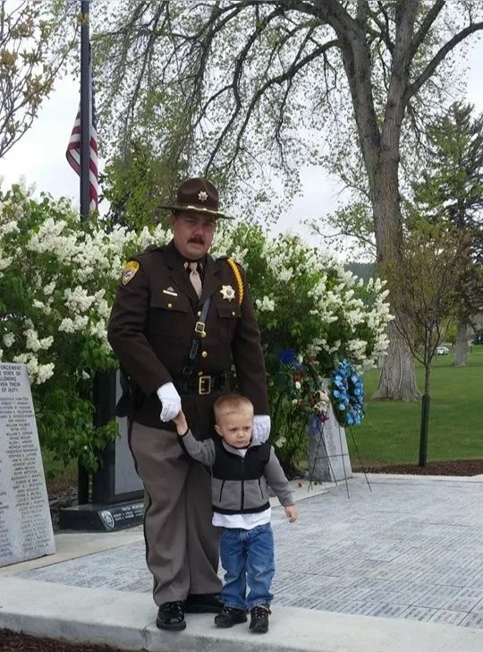 John Looney in Lewis and Clark County Sheriff's Office uniform with a young child at a memorial